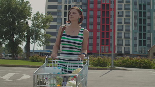 在购物中心附近的停车场穿着裙子的年轻女子推着购物车视频的预览图