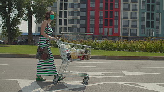 在购物中心附近戴着防护附近戴着防护口罩的年轻女子带着满满的购物车视频的预览图
