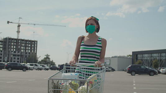 在购物中心附近的停车场戴着防护口罩的年轻女子推着购物车视频的预览图