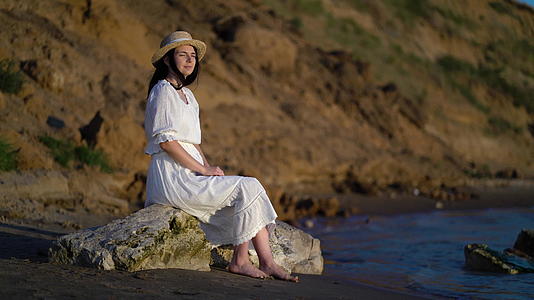 穿着衣服的女人坐在海边的一块大石头上视频的预览图