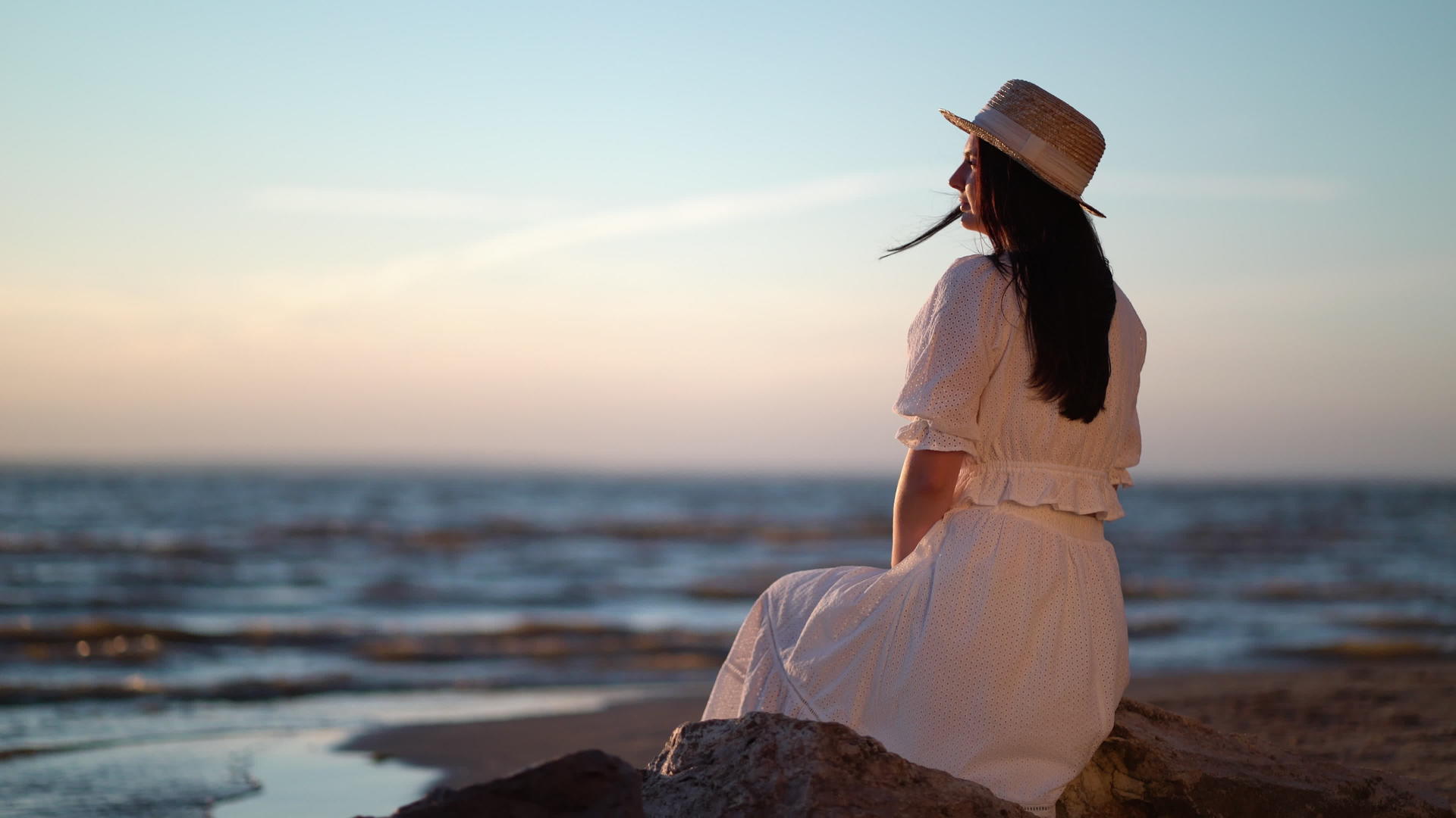穿着衣服的女人坐在海边的一块大石头上视频的预览图