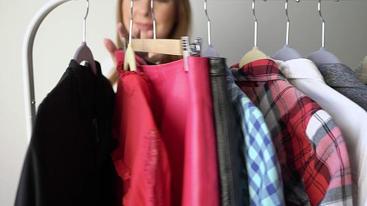 年轻女性在衣架上选择衣服寻找合适的店或衣柜视频的预览图