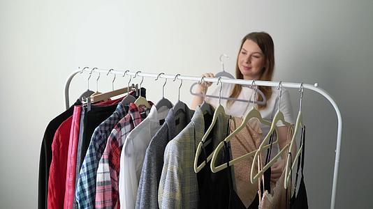 年轻女性在衣架上选择衣服寻找合适的店或衣柜视频的预览图