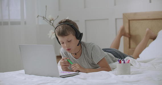 青少年男孩在家里用笔记本电脑在床上的专辑上画彩色和图片视频的预览图