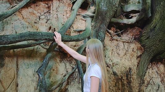 年轻的金发金发女郎仰望着天然沟林中的树根视频的预览图