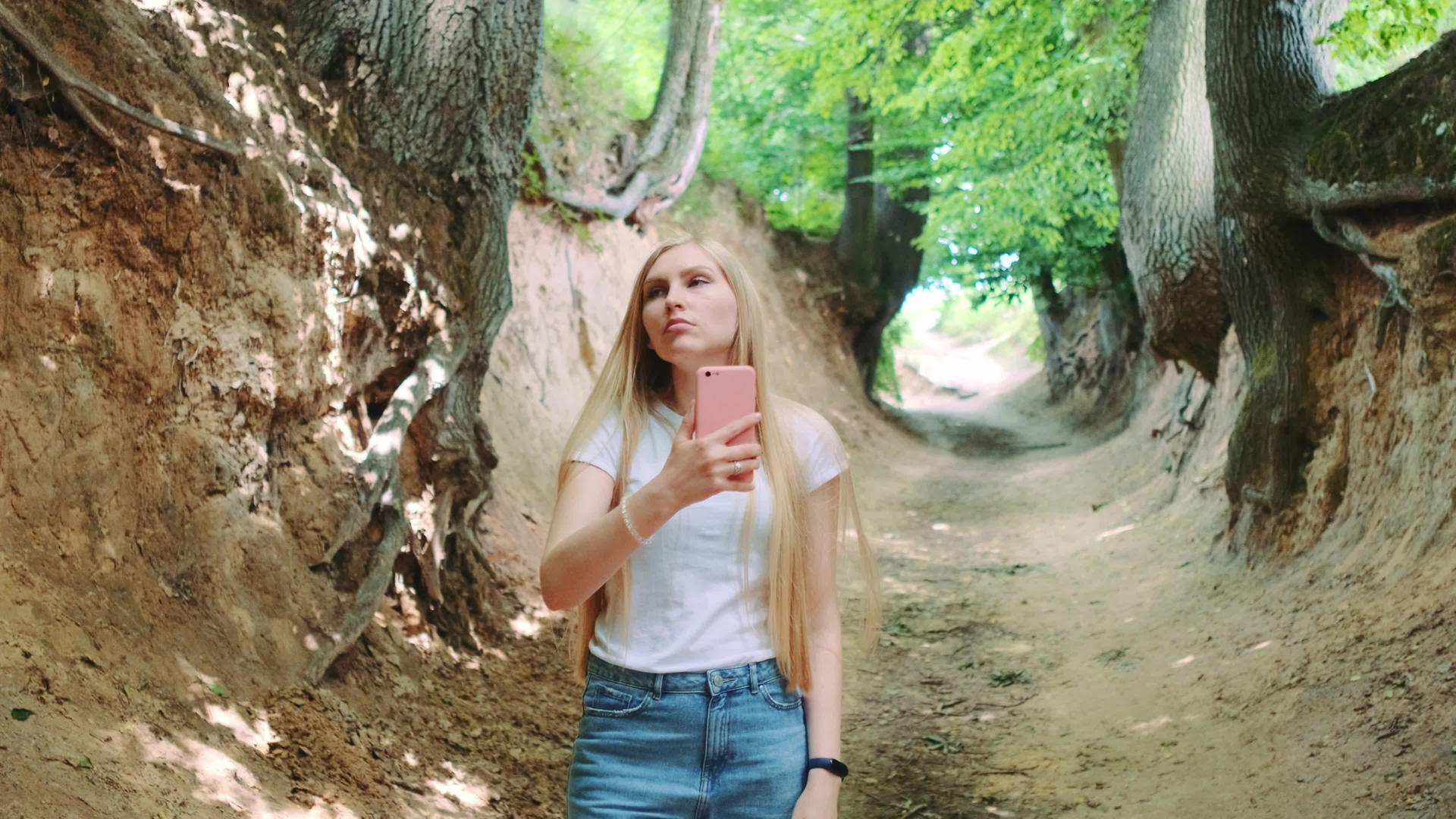 金发碧眼的年轻金发女郎在魔法根峡谷用智能手机拍照视频的预览图