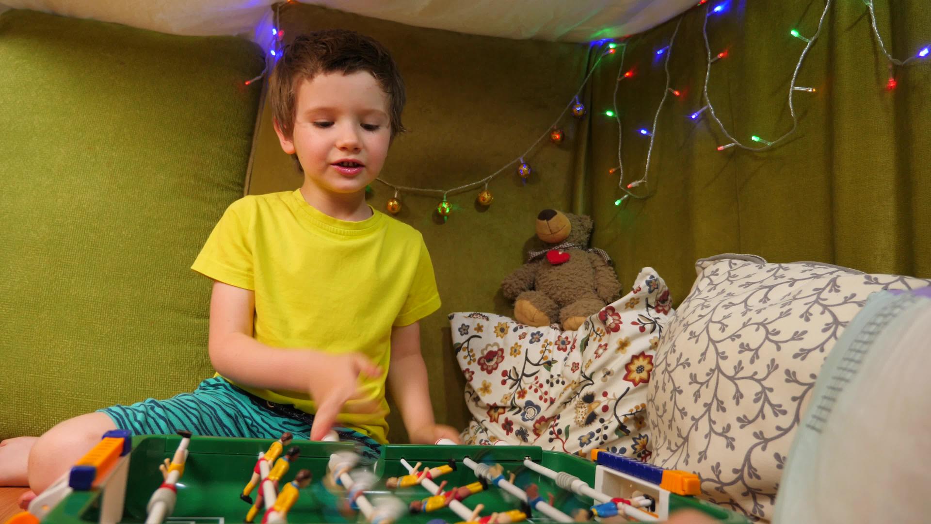 可爱的高加索男孩在一个有毯子和枕头的小房子里玩足球视频的预览图