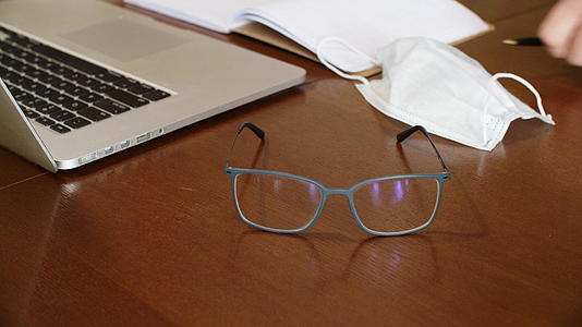 笔记本电脑上木制桌子上的眼镜防护面具和日常规划师的背景工作视频的预览图