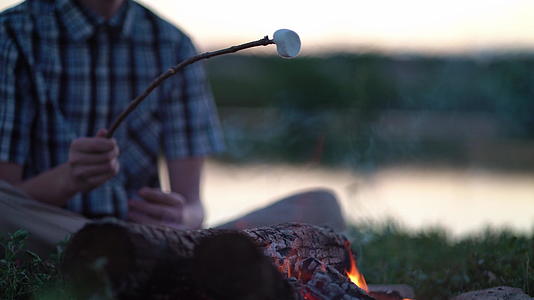 年轻游客在露营附近的火上烤棉花糖视频的预览图
