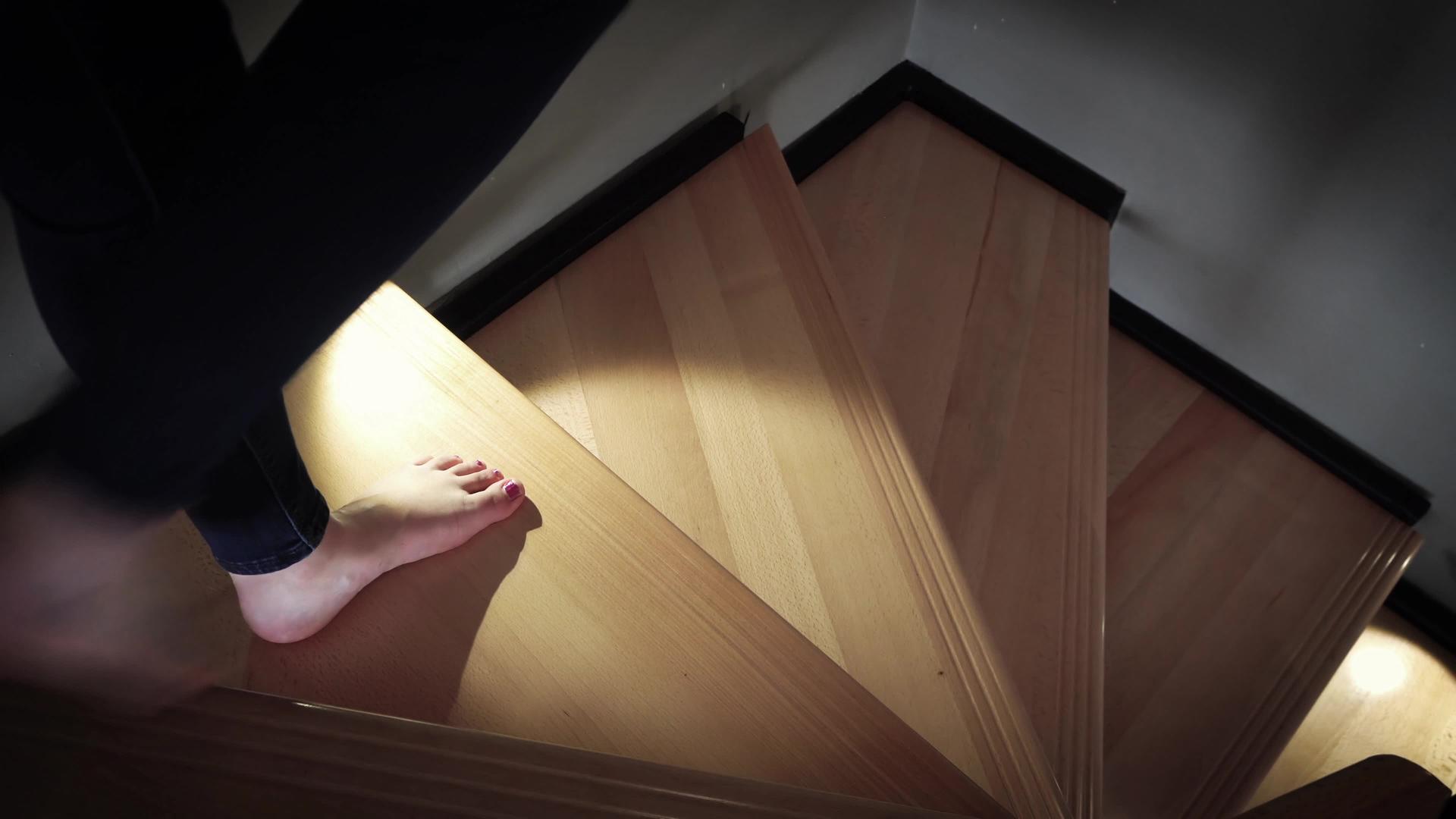 一个赤脚的女人在豪华的房子里走过木楼梯晚上被灯光照亮视频的预览图