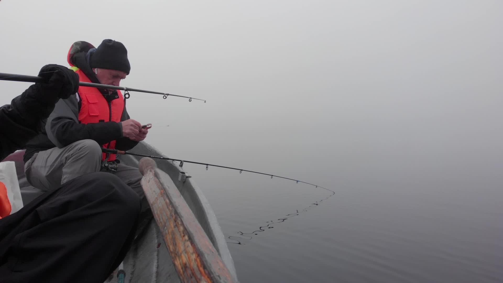 两个白人男子在芬兰湖浓雾中用棍子从船上钓鱼视频的预览图