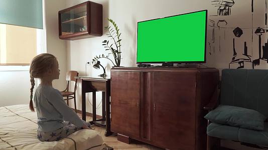坐在旧家具装饰卧室的床上用绿屏在床上观看LcdTv视频的预览图