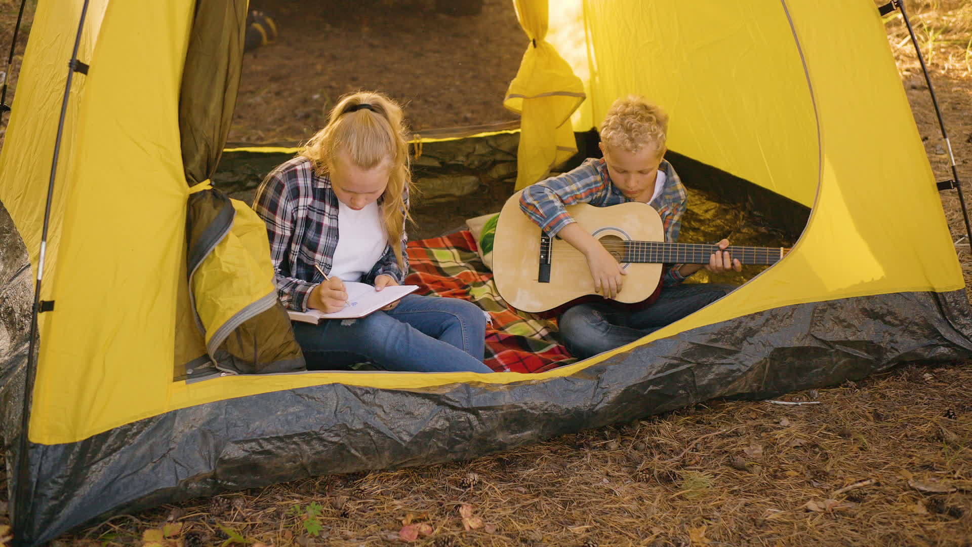 一个十几岁的男孩拿着吉他坐在露营帐篷里年轻女孩在森林里视频的预览图
