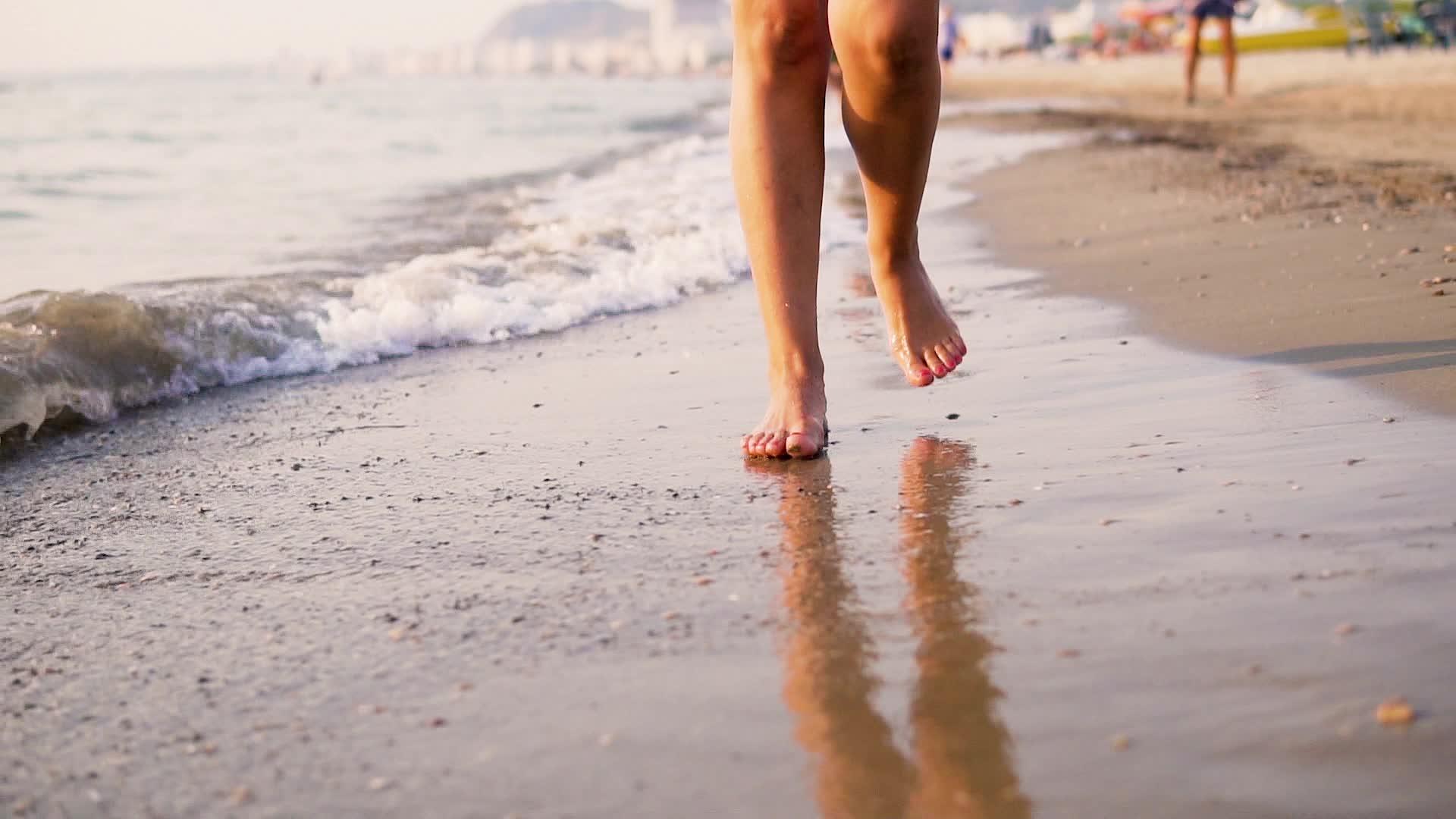 年轻女子的腿踩在海滩上海浪缓缓飘动视频的预览图