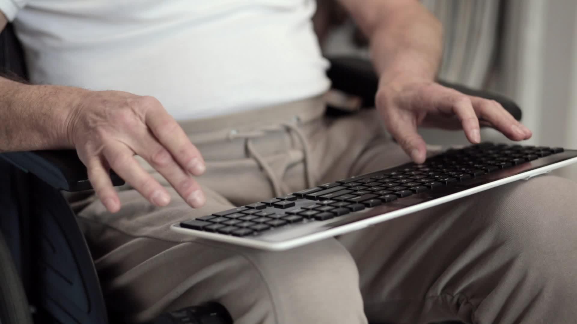 一名成年男子坐在轮椅上打字时手持键盘视频的预览图