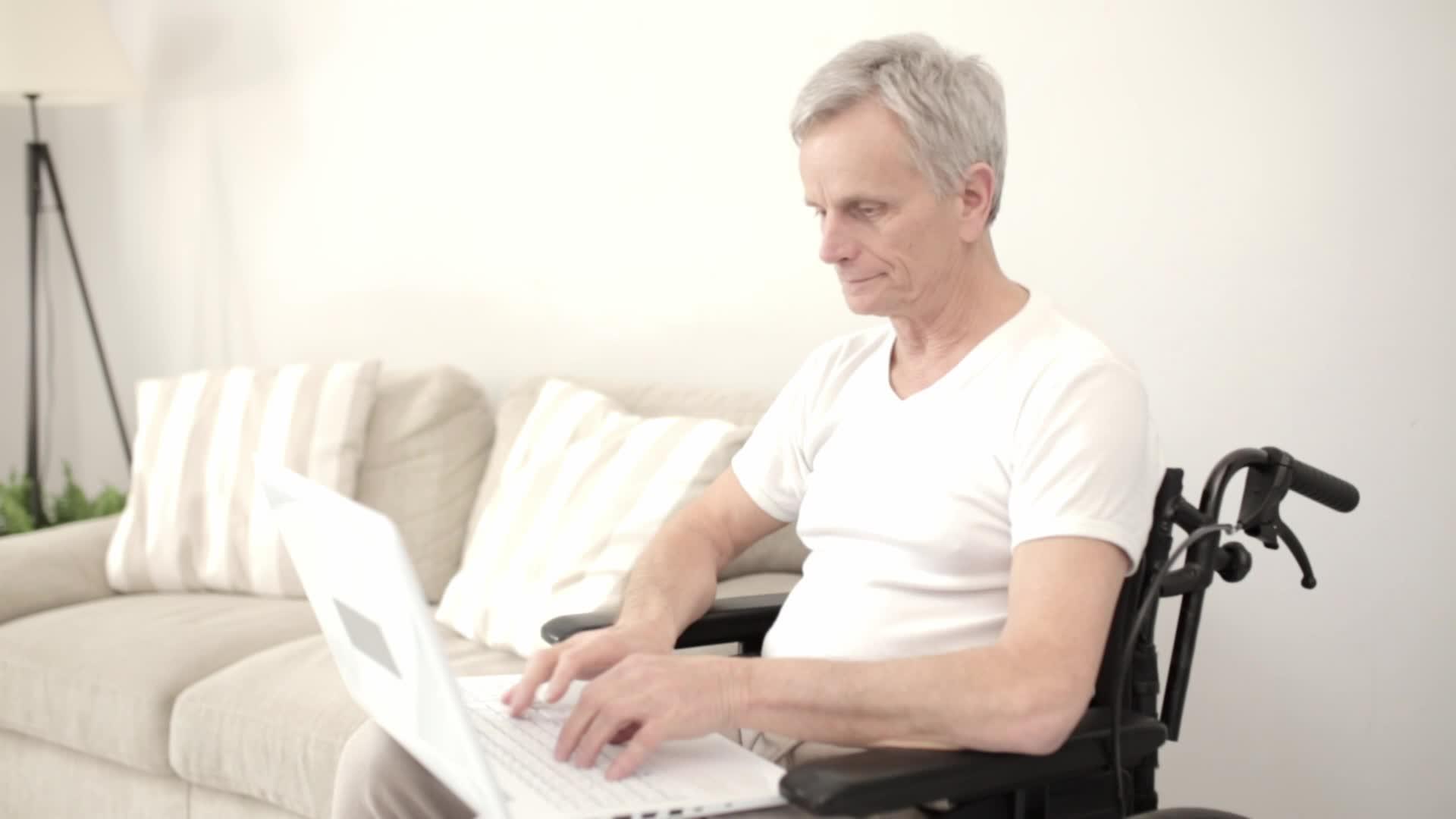 坐在笔记本电脑旁边的白发男子坐在病房的轮椅上视频的预览图