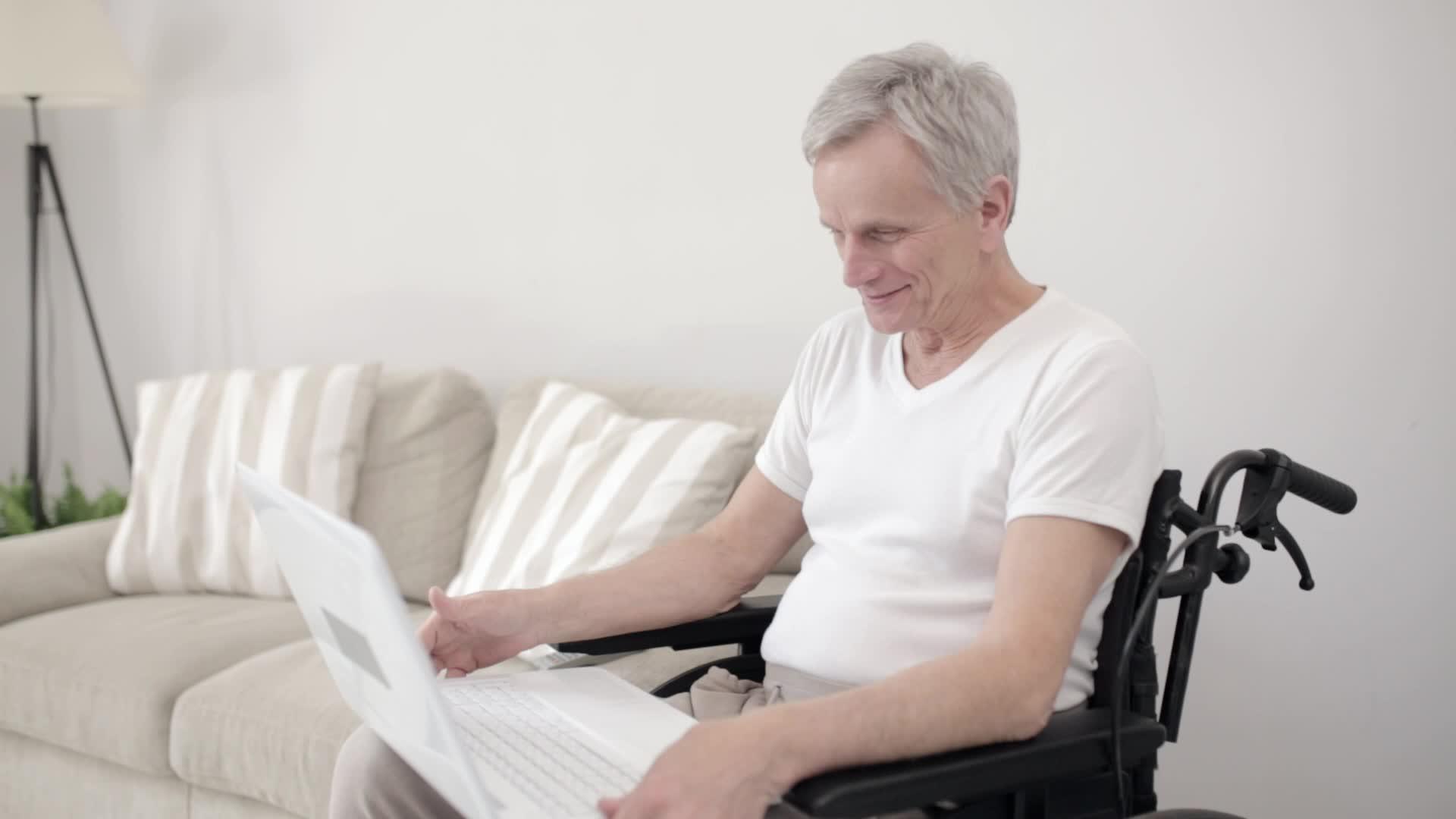 一名灰色头发的男子穿着轮椅和家人在当地医院的房间里视频的预览图
