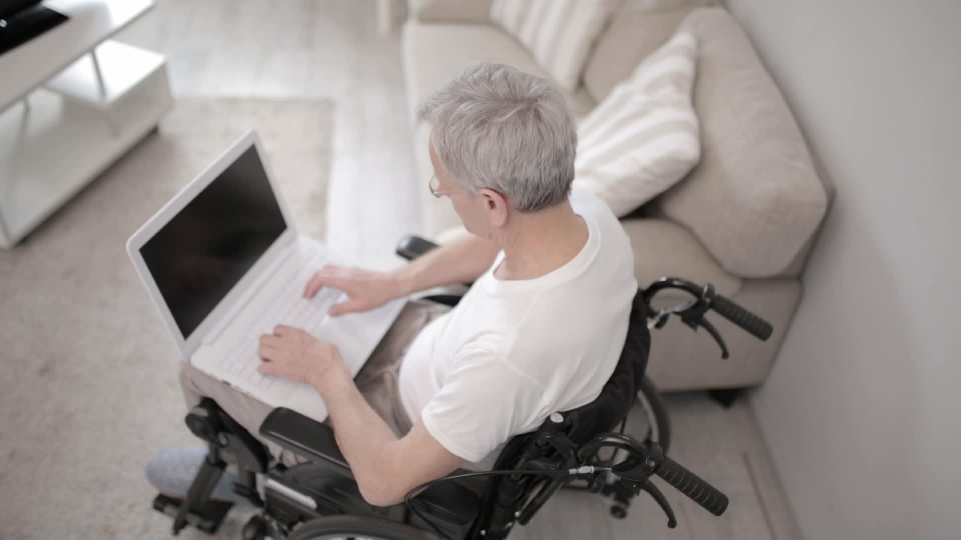 坐在笔记本电脑旁边的白发男子坐在病房的轮椅上视频的预览图