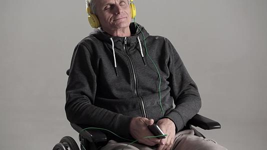 一个坐在轮椅上的灰色头发用耳机听他最喜欢的音乐视频的预览图
