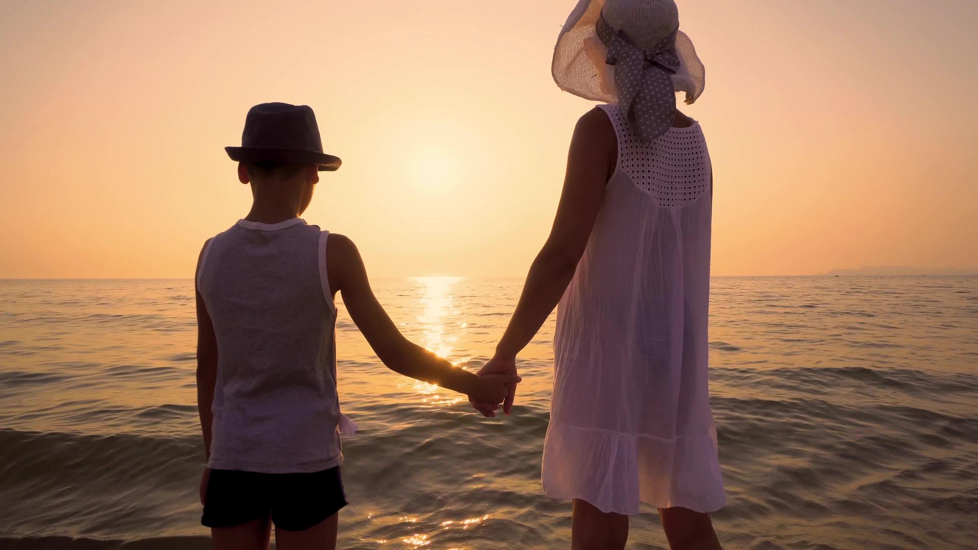 母亲和儿子戴着帽子站在日落的海滩上Standicam视频的预览图