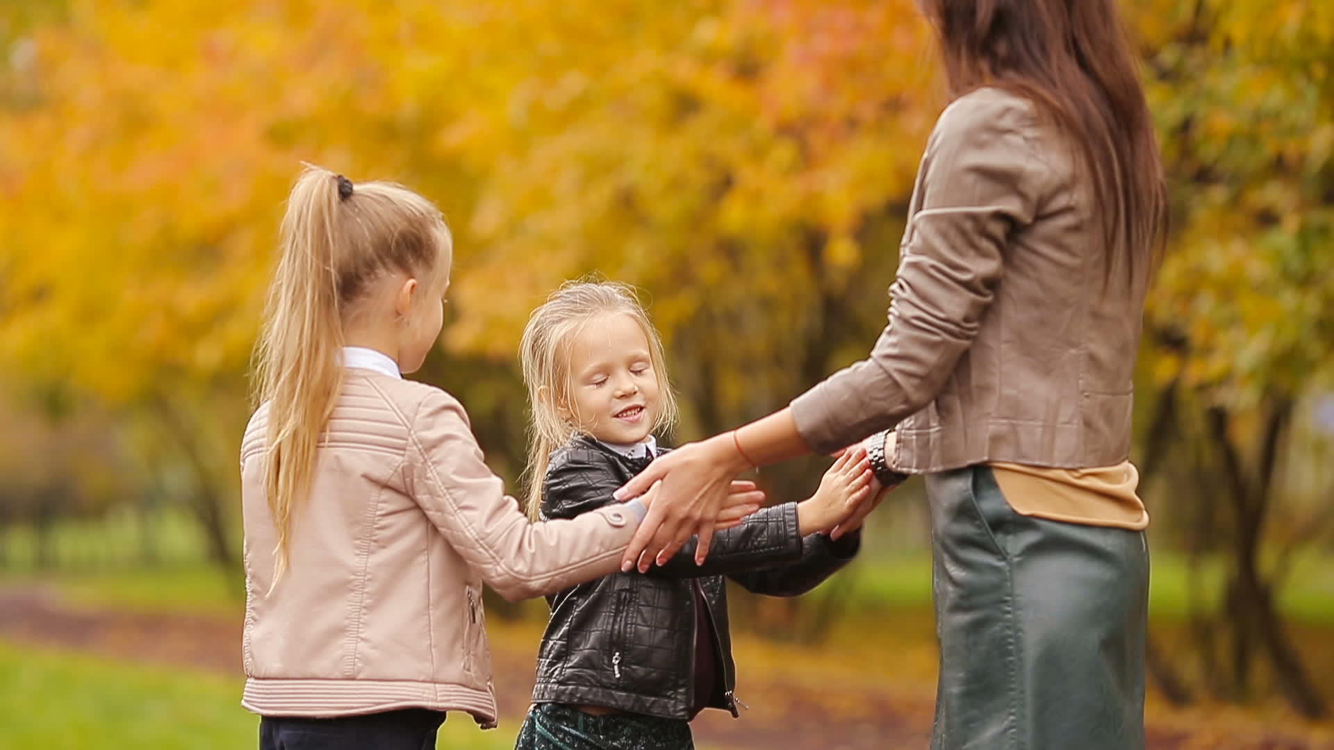 年轻的母亲和两个女儿在秋天的公园里玩游戏视频的预览图