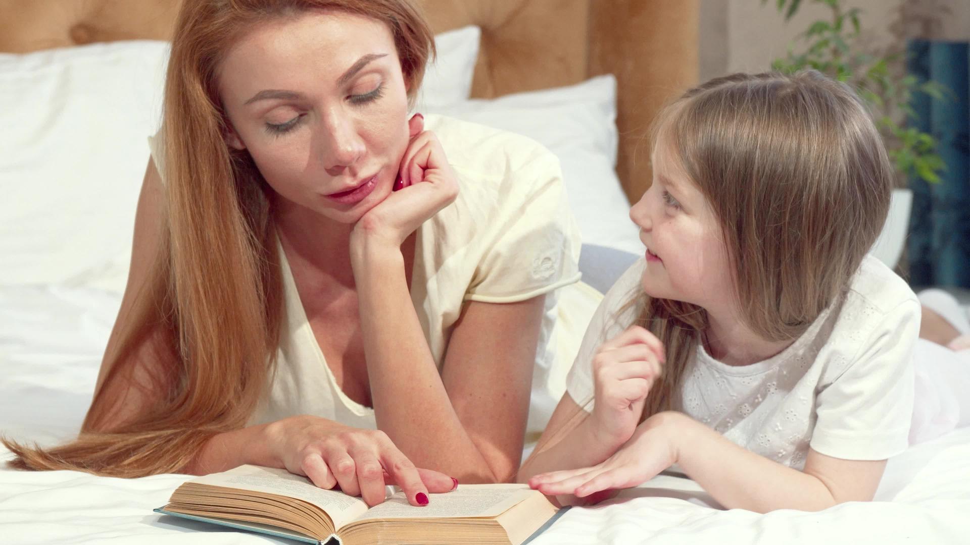 美丽的女人和可爱的小女儿一起看书躺在家里的床上睡觉视频的预览图