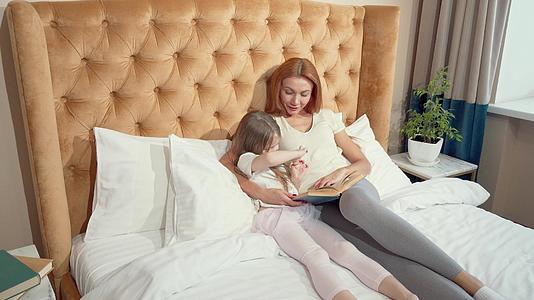 母亲和女儿正在看一本书一张躺在床上的照片视频的预览图