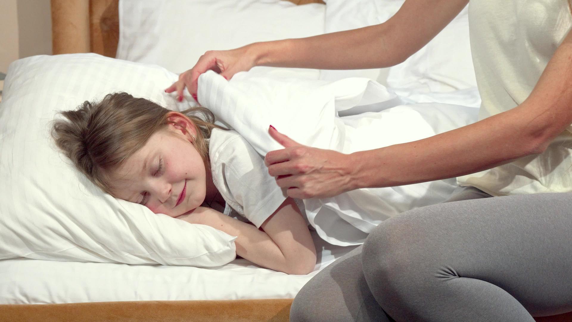 那个无法辨认的女人把毯子塞在毯子上为她睡着的女儿视频的预览图