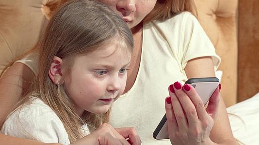 这个可爱的小女孩用智能手机和她妈妈一起打电话视频的预览图