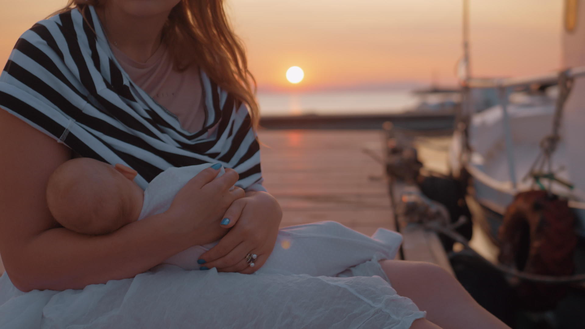 日落时坐在码头的婴儿哺乳和抚养母亲视频的预览图