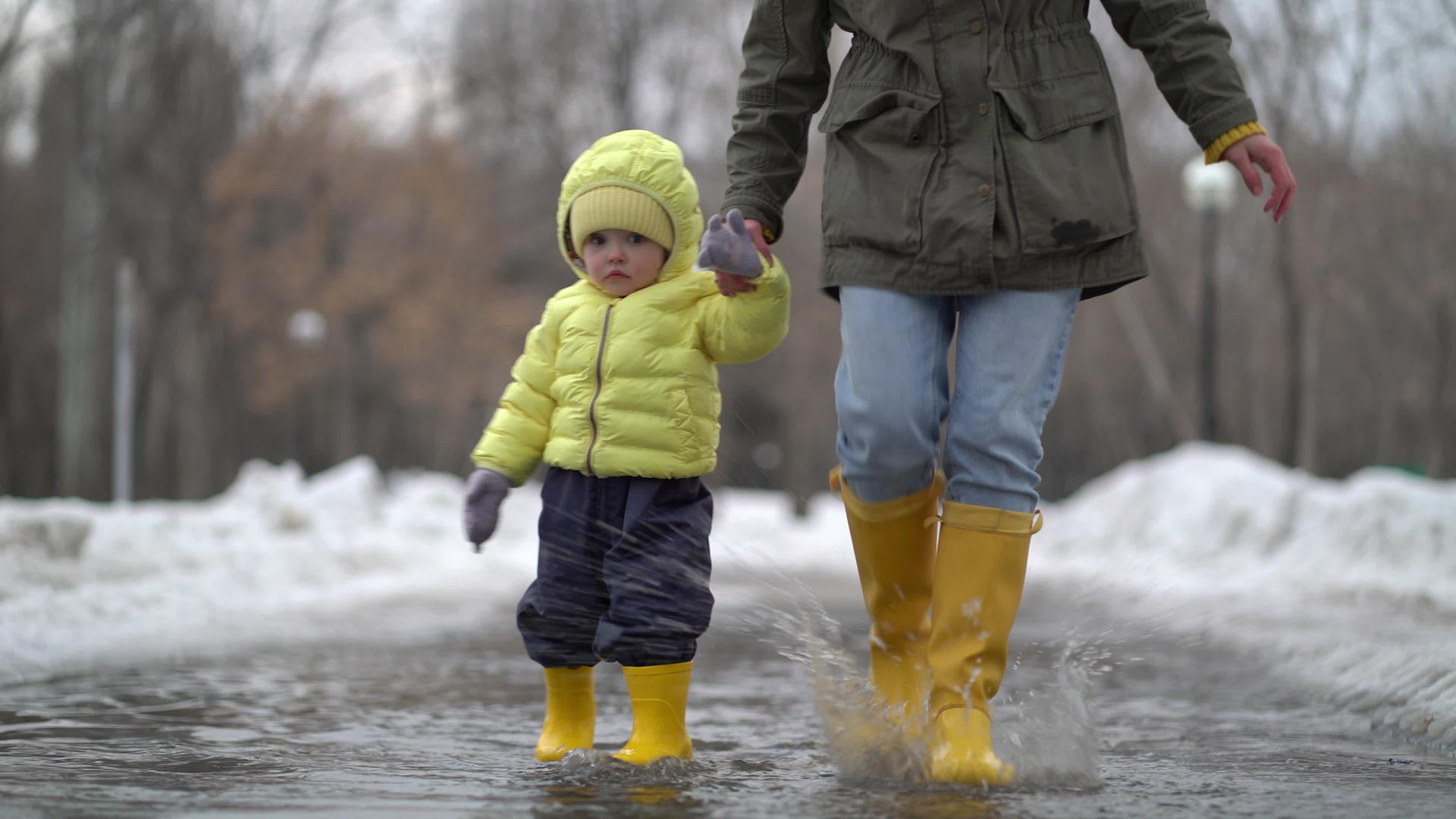 母亲和女儿穿着黄色橡胶靴在水坑里行走视频的预览图