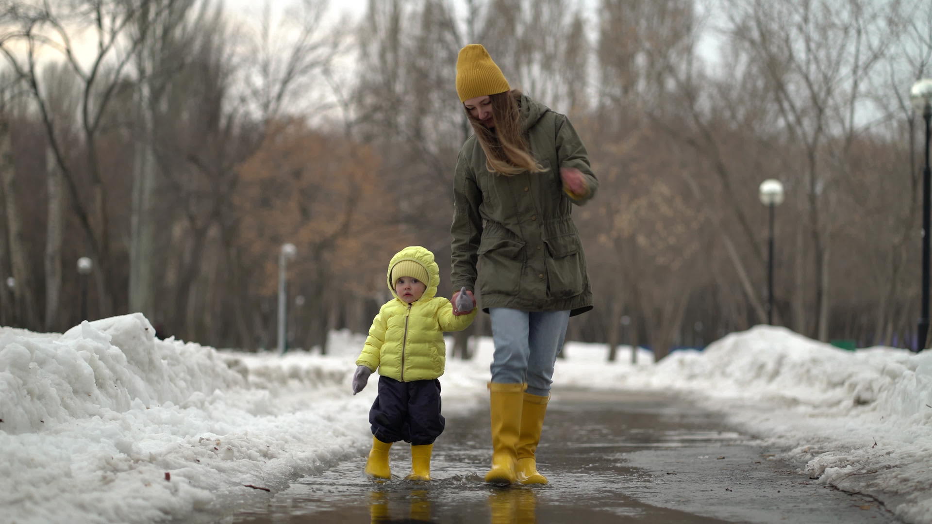母亲和女儿穿着黄色橡胶靴在水坑里行走视频的预览图