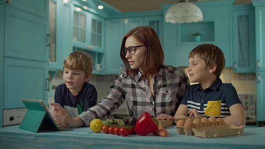 一家人一起做饭看着站在蓝色厨房的平板电脑上的在线食谱视频的预览图