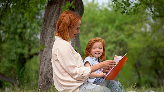母亲和女孩坐在树下看书视频的预览图