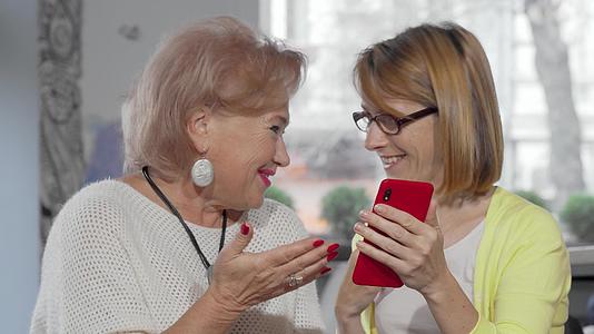 在她的智能手机上一位成年女子向年长的母亲展示了一些东西视频的预览图