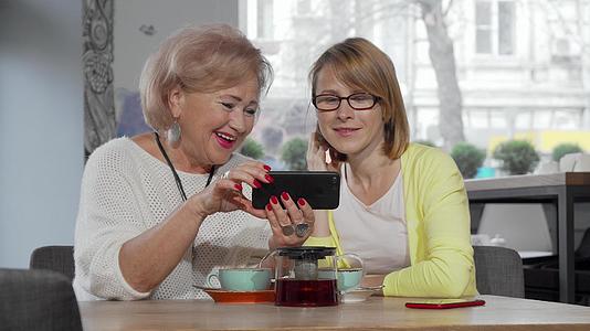 成熟的妇女和她的老母亲在咖啡馆里使用智能手机视频的预览图