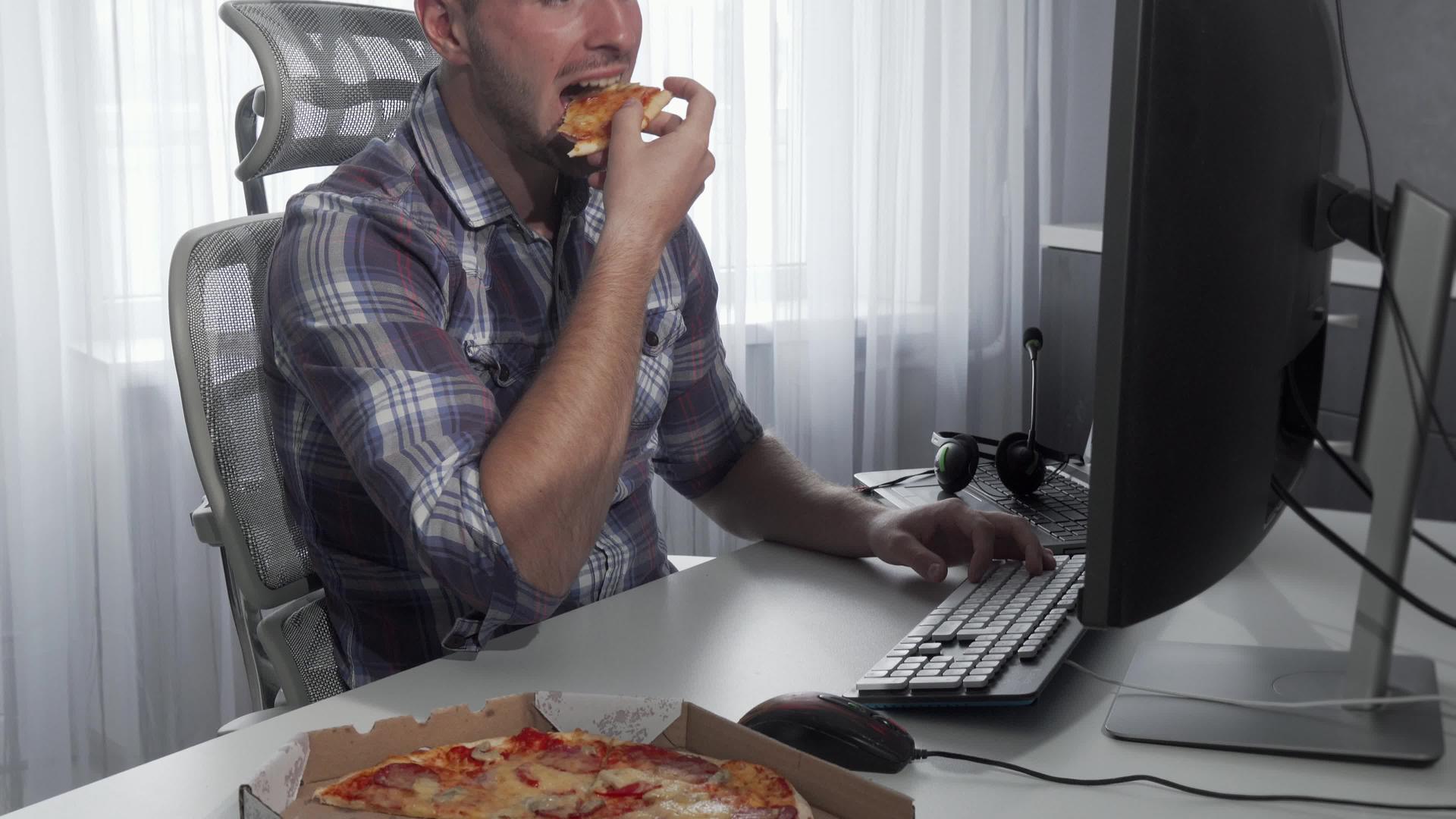 英俊的男人在电脑上工作时享受美味的披萨视频的预览图