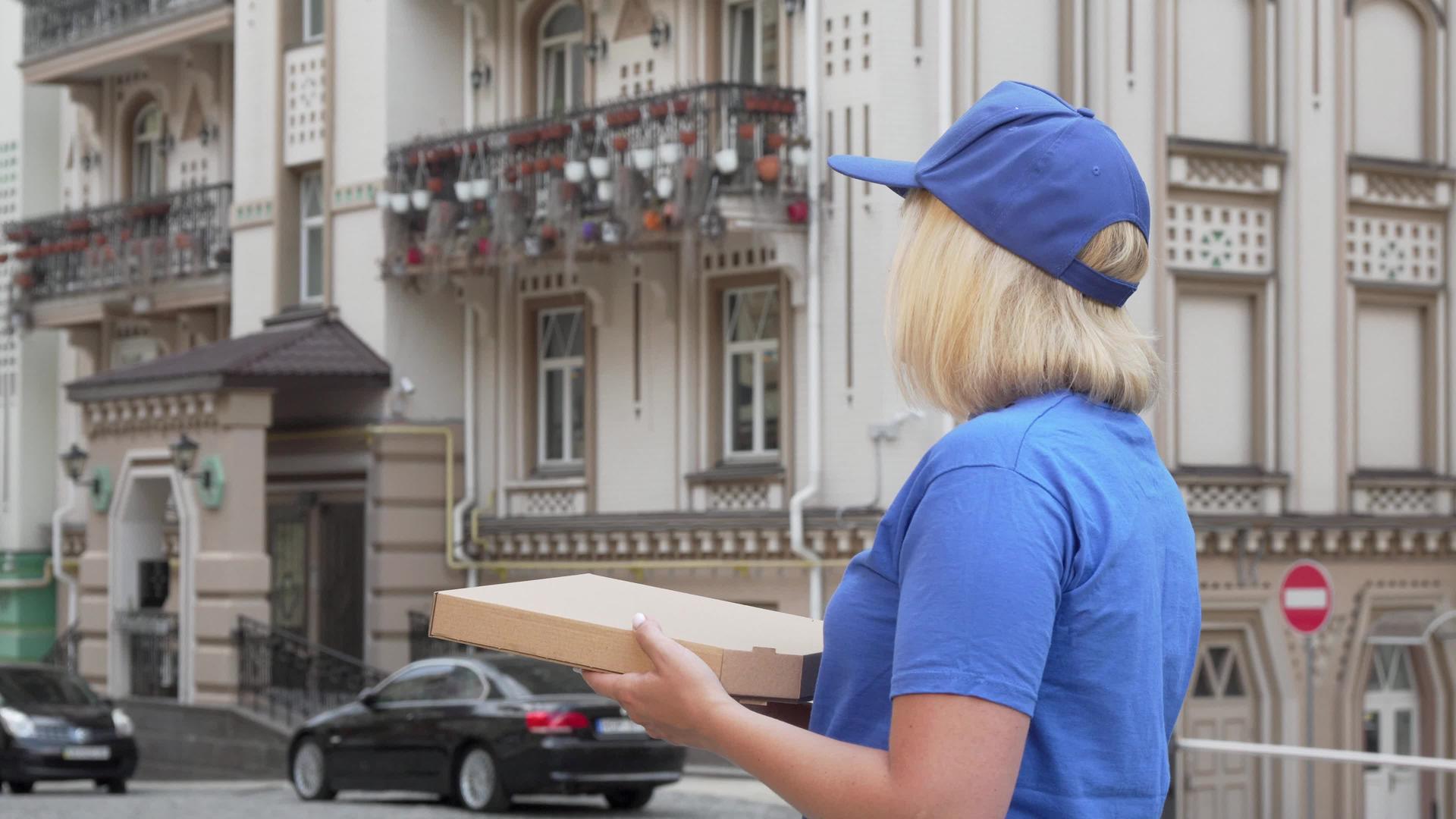 一个送货的女人看着街上拿着披萨盒的街背视频的预览图