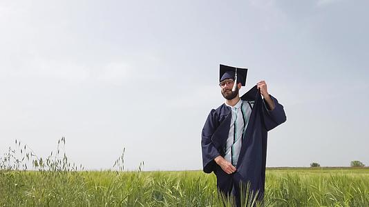 一个从绿色田野毕业的男人脱下衣服扔下蓝帽子和礼服视频的预览图