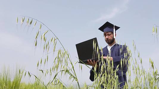 一个从田野毕业的人看着笔记本电脑扔蓝帽子虚拟毕业视频的预览图