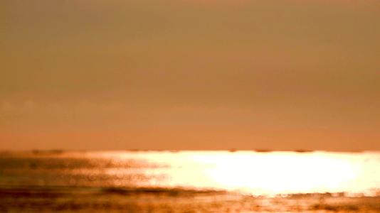 海面上明亮的阳光和小浪移动时的模糊反射橙色视频的预览图