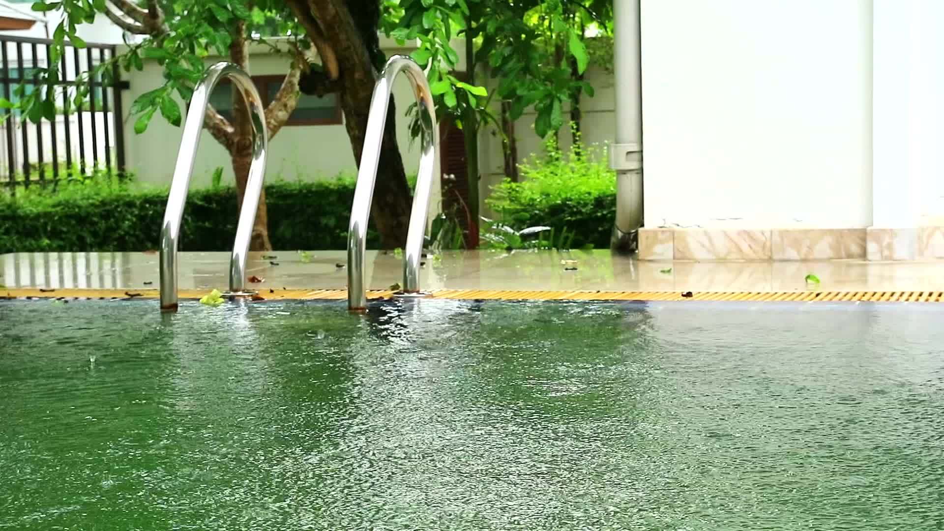 雨水落在不锈钢楼梯和绿色花园背景附近的池塘水面上视频的预览图