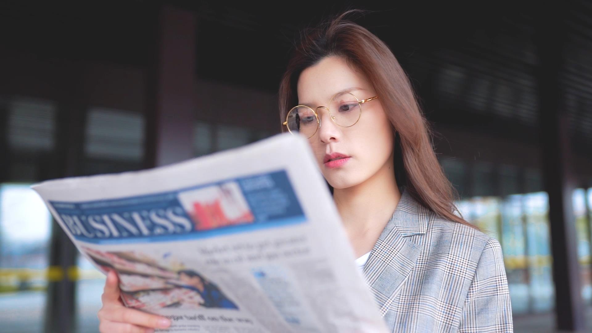 戴眼镜的女生站在金融大楼下看报纸视频的预览图