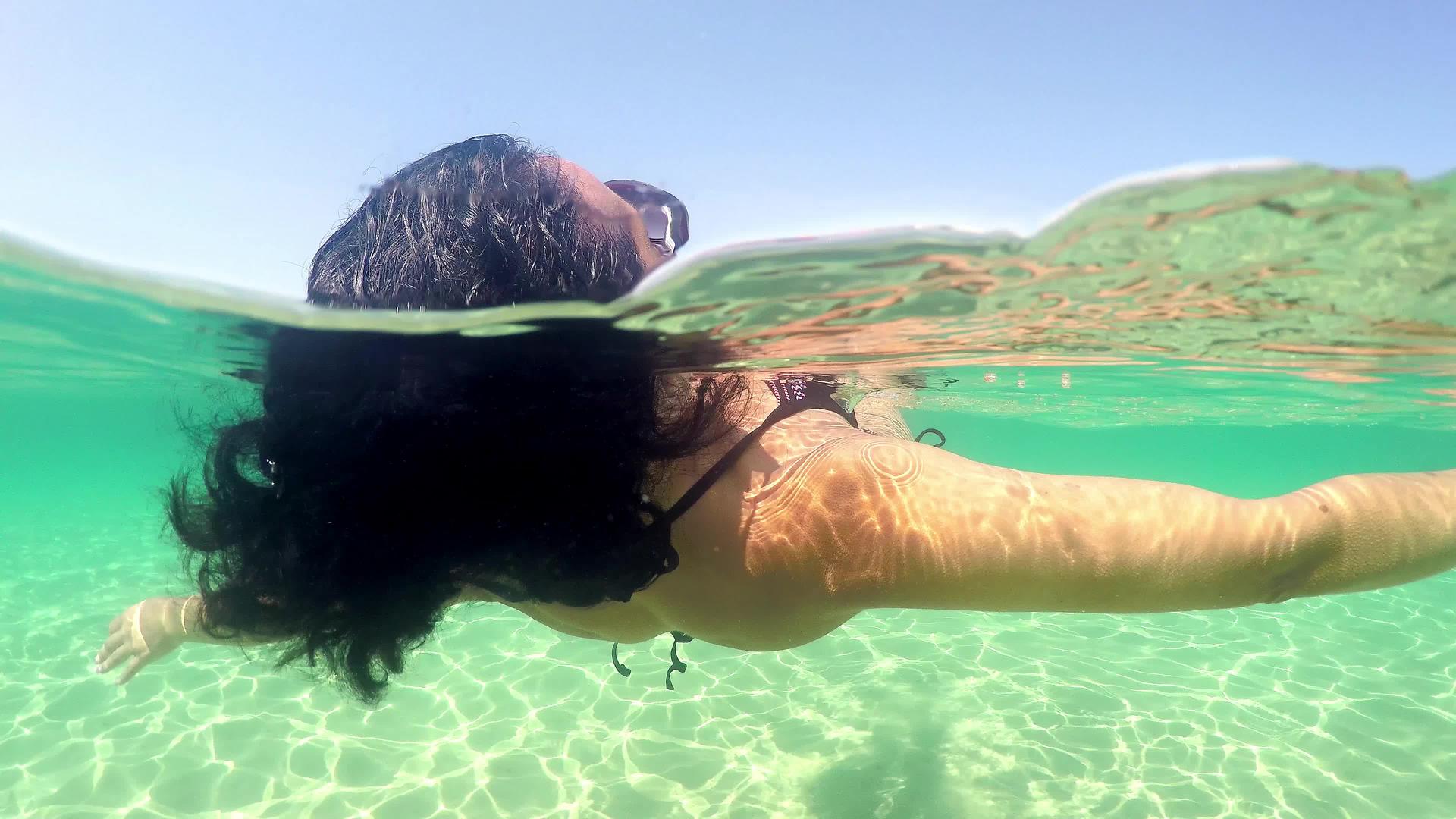 黑色卷发的女人穿着性感的泳衣漂浮在平静的水面上视频的预览图