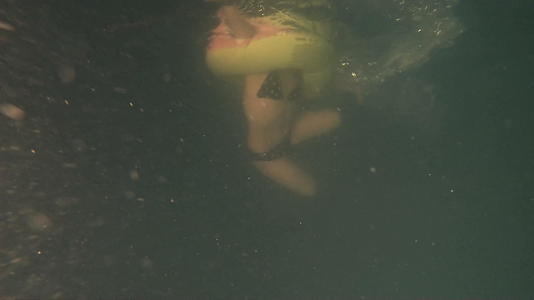 带着充气环的小女孩带着微粒在深黑肮脏的游泳池里游泳在水下慢慢移动视频的预览图