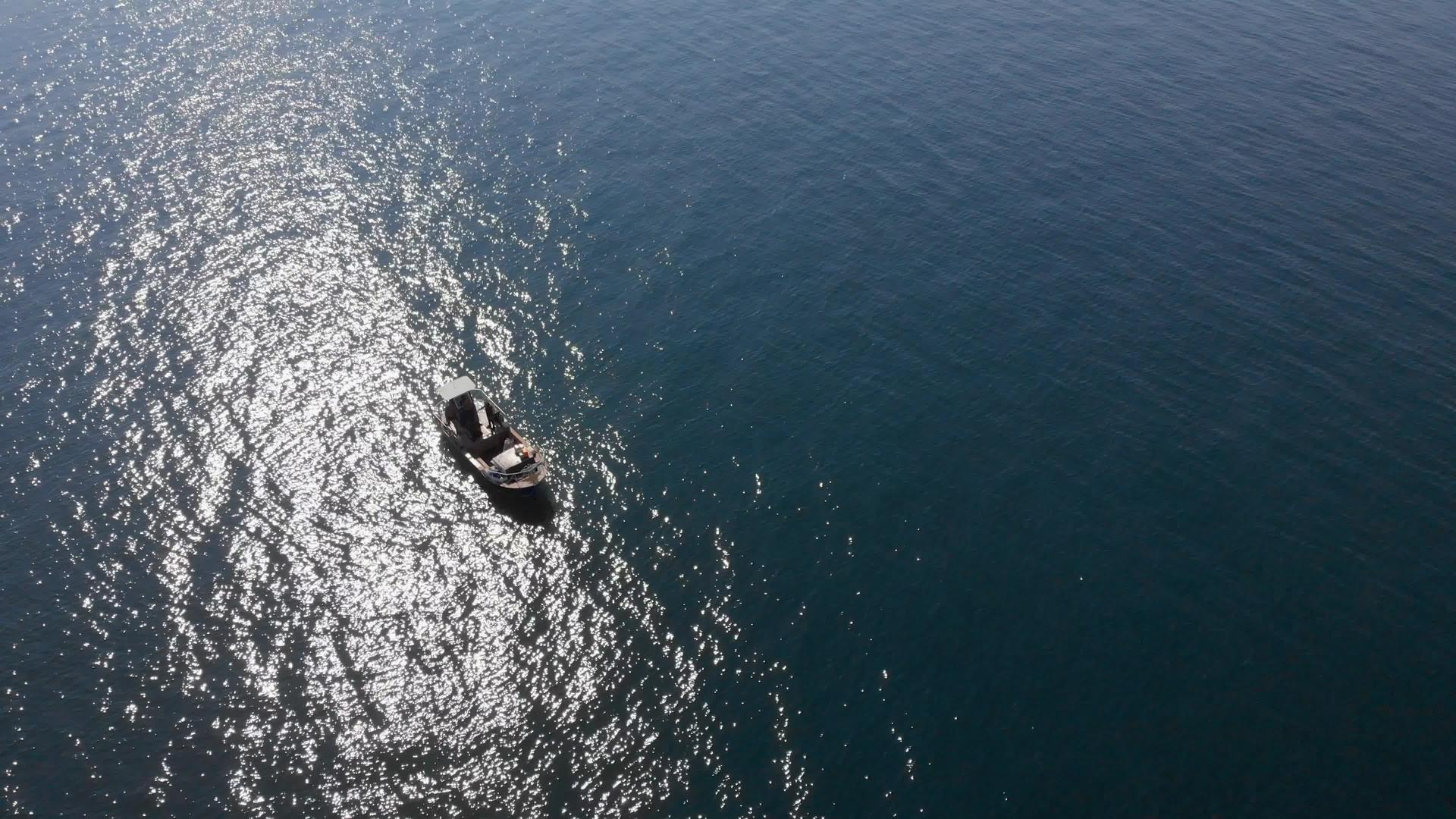 小渔船在蓝色的海水中的空中背光阳光和波光粼粼的水面视频的预览图