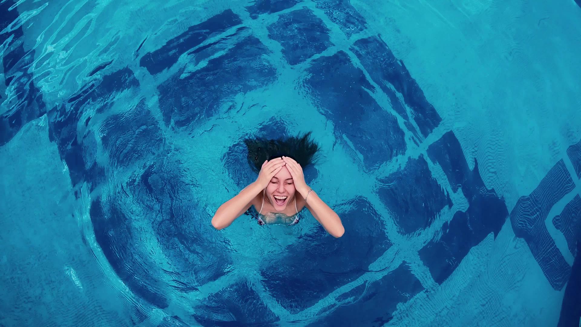 一个开朗的年轻女子在她的后院游泳池里放松穿着粉红色的比基尼视频的预览图