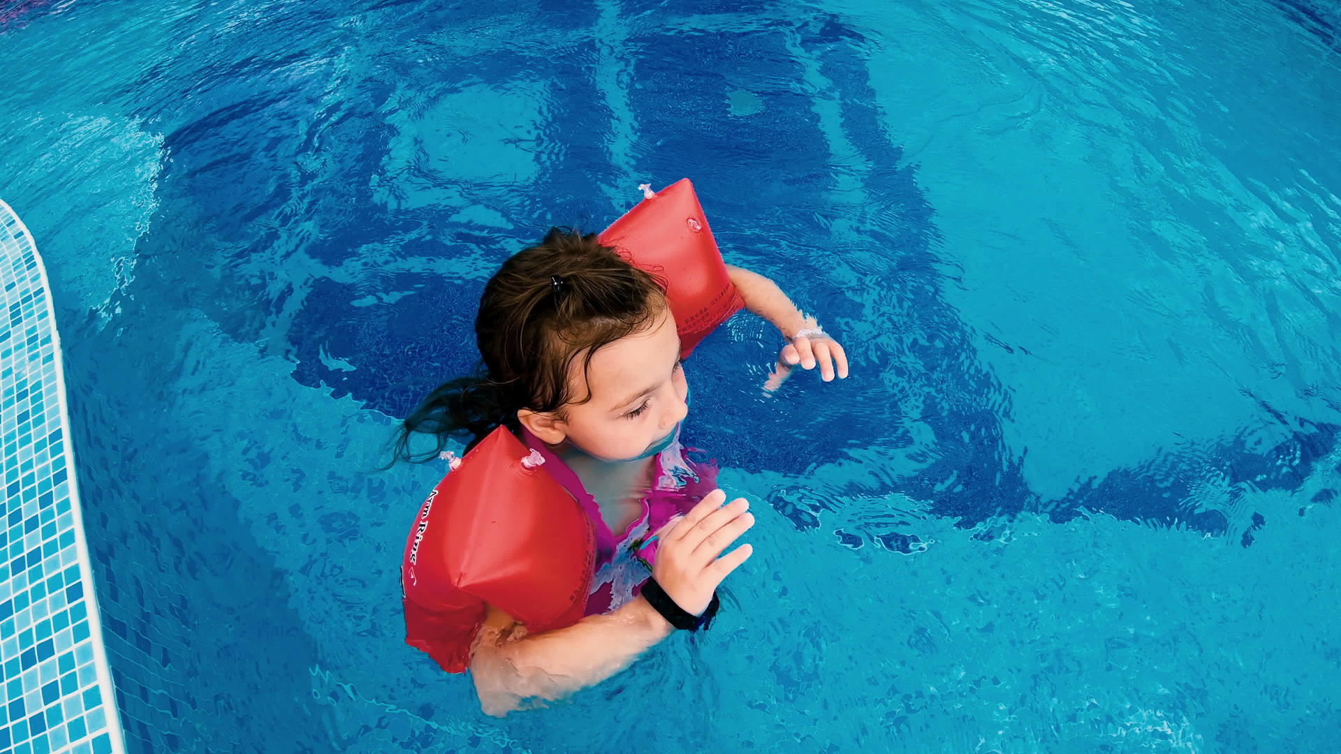 快乐的小女孩在游泳池里充满了充气的手臂放松微笑着视频的预览图