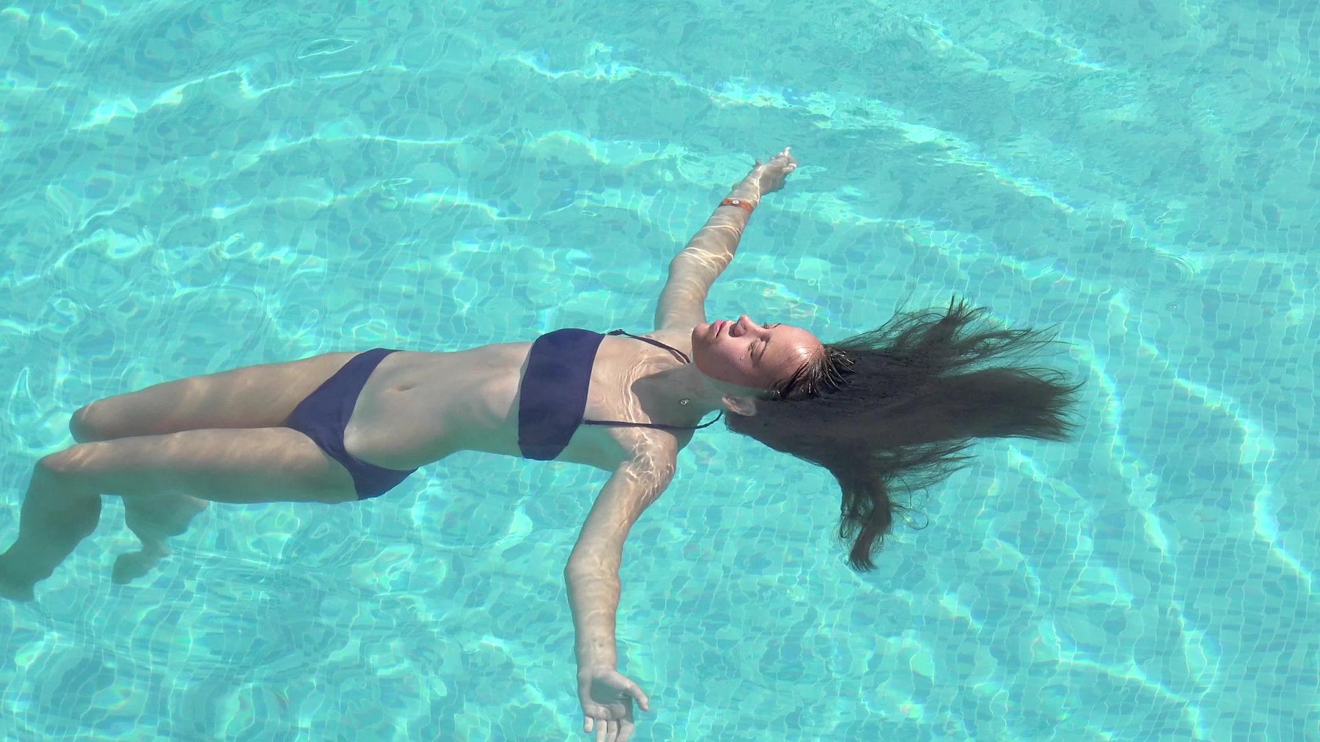 年轻女子躺在水晶清澈的游泳池里在空中游泳视频的预览图