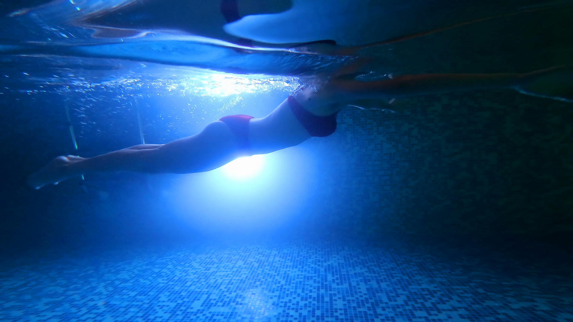 一个漂亮的女孩在水下游泳一直游到晚上有灯光的水池女人们被淹没在水下直到晚上有一个有灯的水池LED视频的预览图